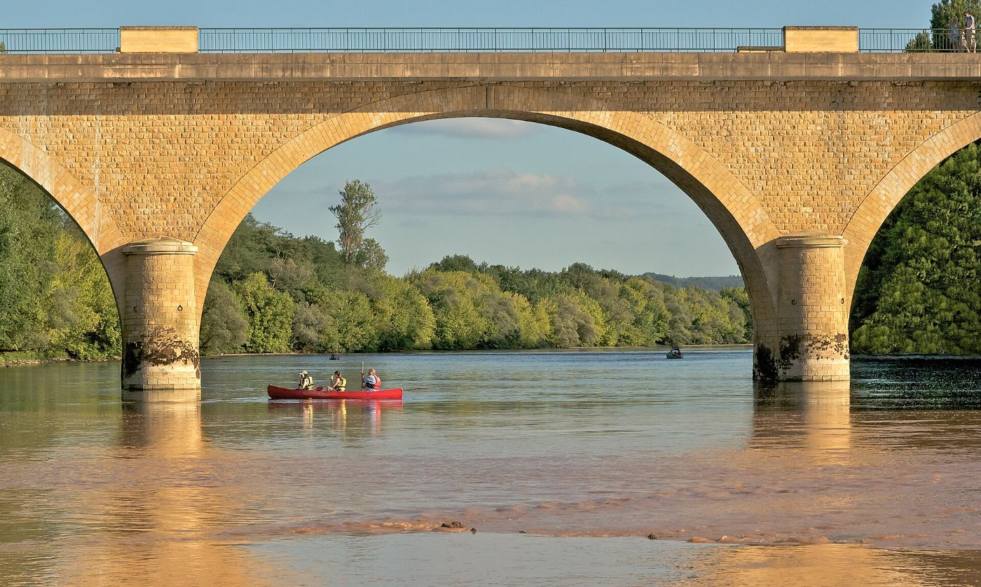 Un canoë passant sous les arches d’un pont de pierre sur la Dordogne